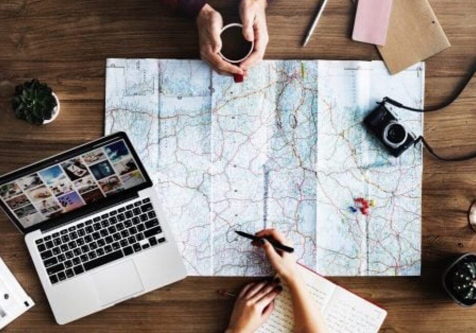 Two people planning a trip with a map, laptop, and camera on a table
